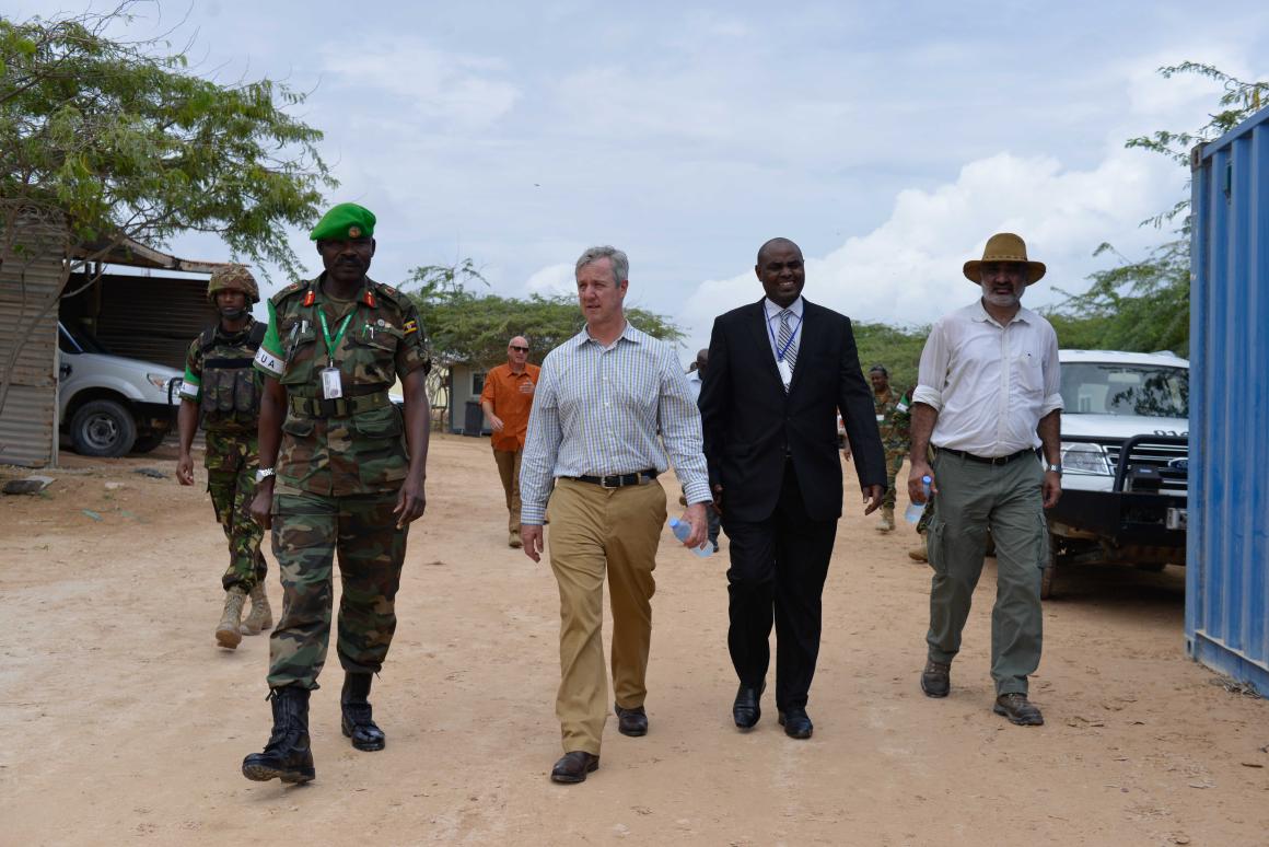 Five men walk down a dirt road, two in military uniform. 